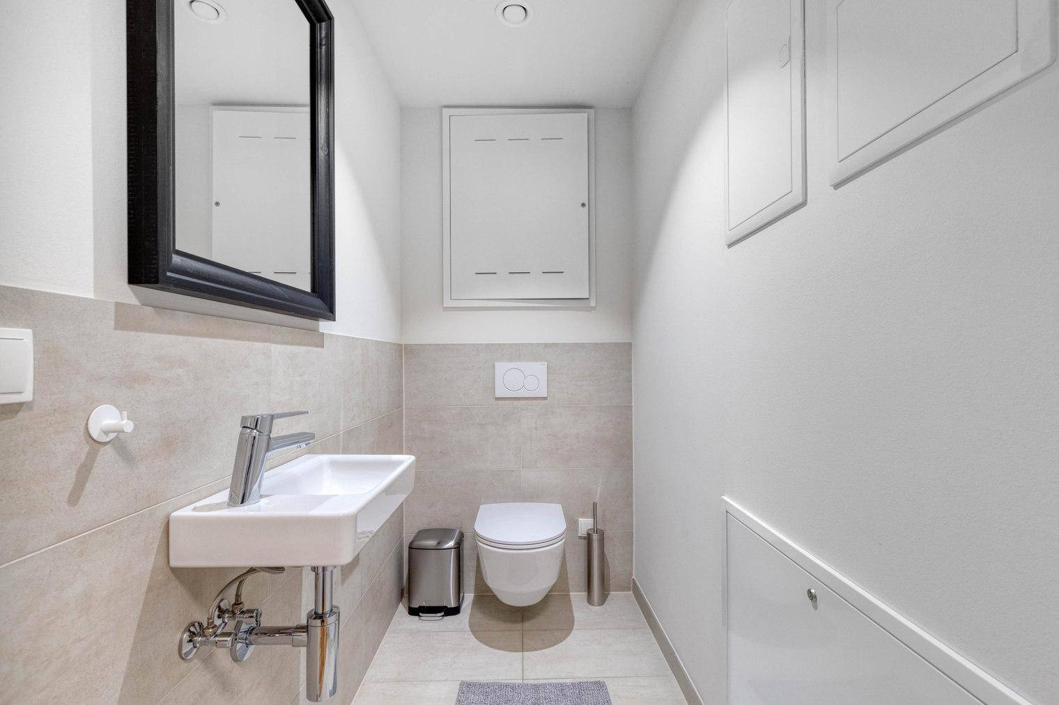 Separates WC mit wandhängender Toilette, kleinem Waschbecken und Spiegel.