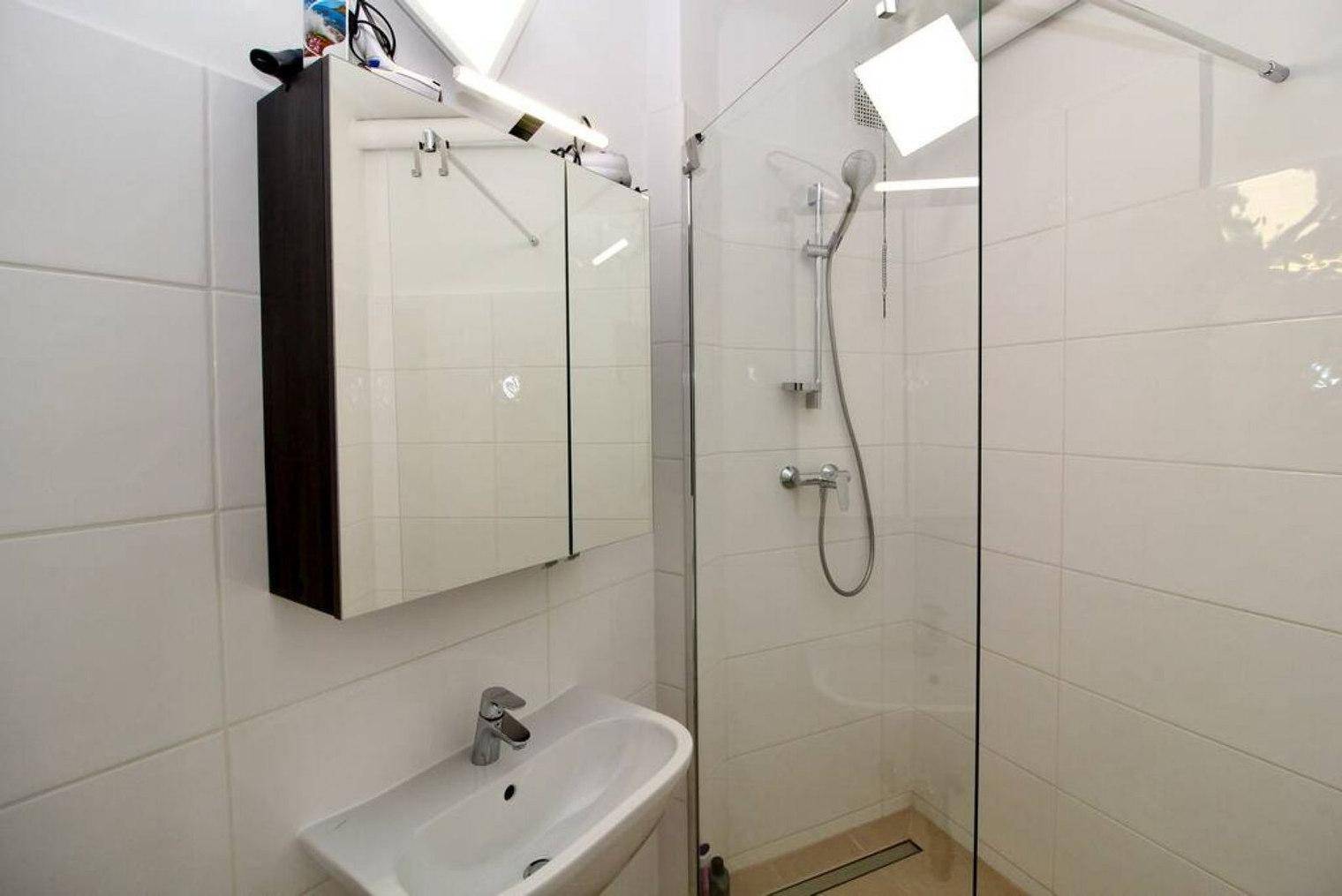 Modernes Badezimmer mit weißen Fliesen, Waschbecken und ebenerdiger Dusche.