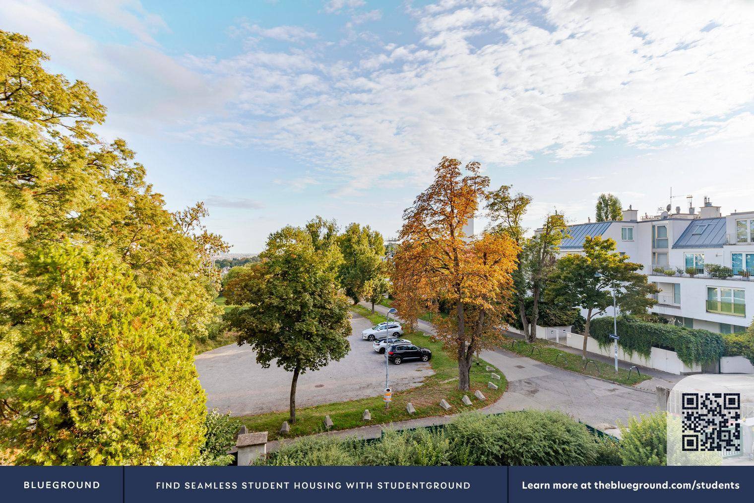 Weitläufiger Blick über grüne Bäume, einen Parkplatz und umliegende Wohngebäude.