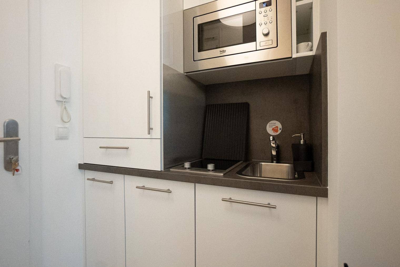 Kompakte Küchenzeile mit Mikrowelle, Kochfeld und Spüle in modernem, weißem Design.