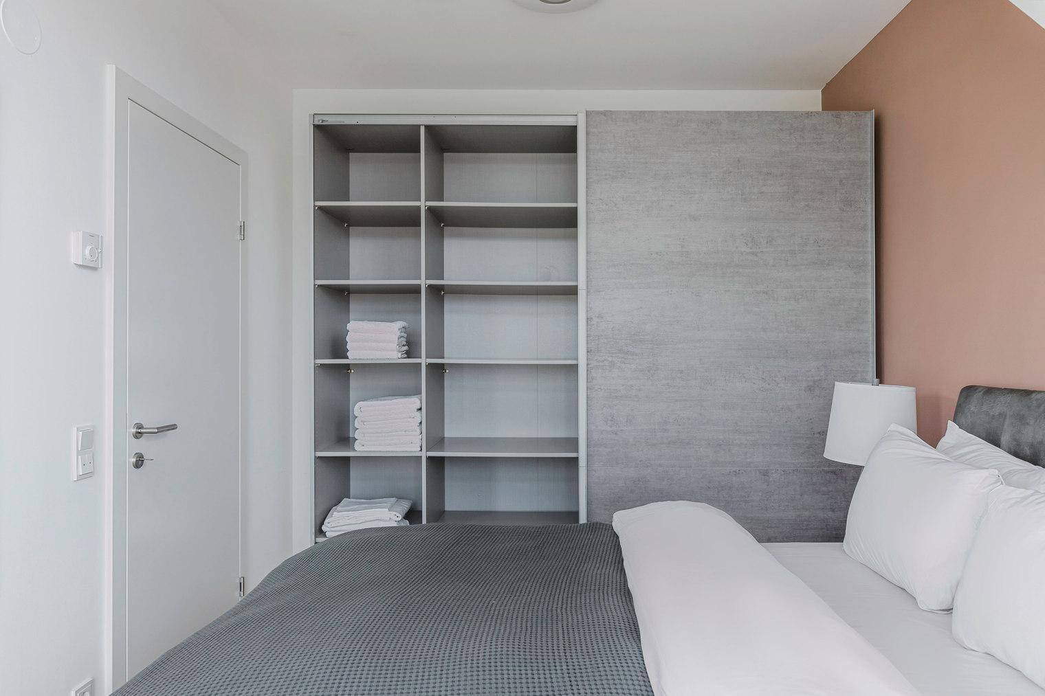 Schlafzimmer mit integriertem Regal und Schiebetürenschrank, ergänzt durch eine rosafarbene Wand.