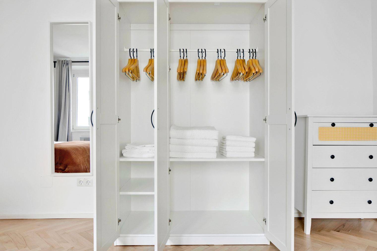 Offener weißer Kleiderschrank mit Kleiderbügeln und gefalteten Handtüchern.