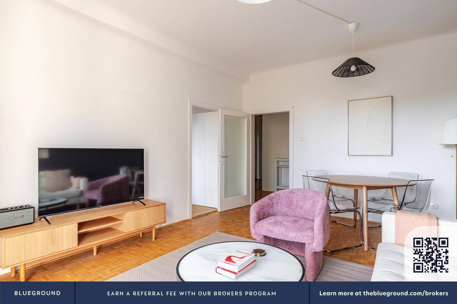 Geräumiger Wohn-Essbereich mit Holzboden, Fernseher und Esstisch mit transparenten Stühlen.