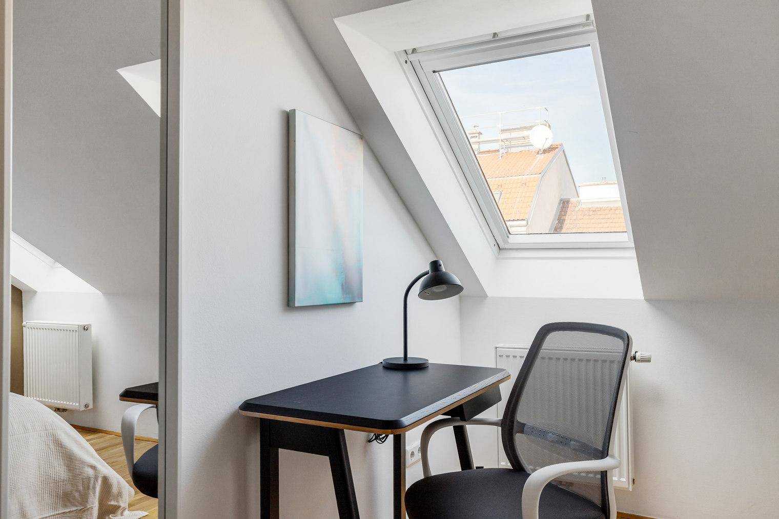 Arbeitsbereich im Schlafzimmer mit Schreibtisch, Bürostuhl und Blick durch das Dachfenster.