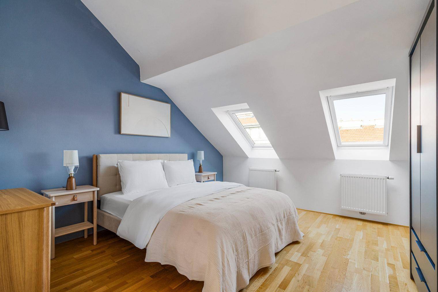 Geräumiges Schlafzimmer im Dachgeschoss mit Doppelbett, blauer Akzentwand und Dachfenstern.