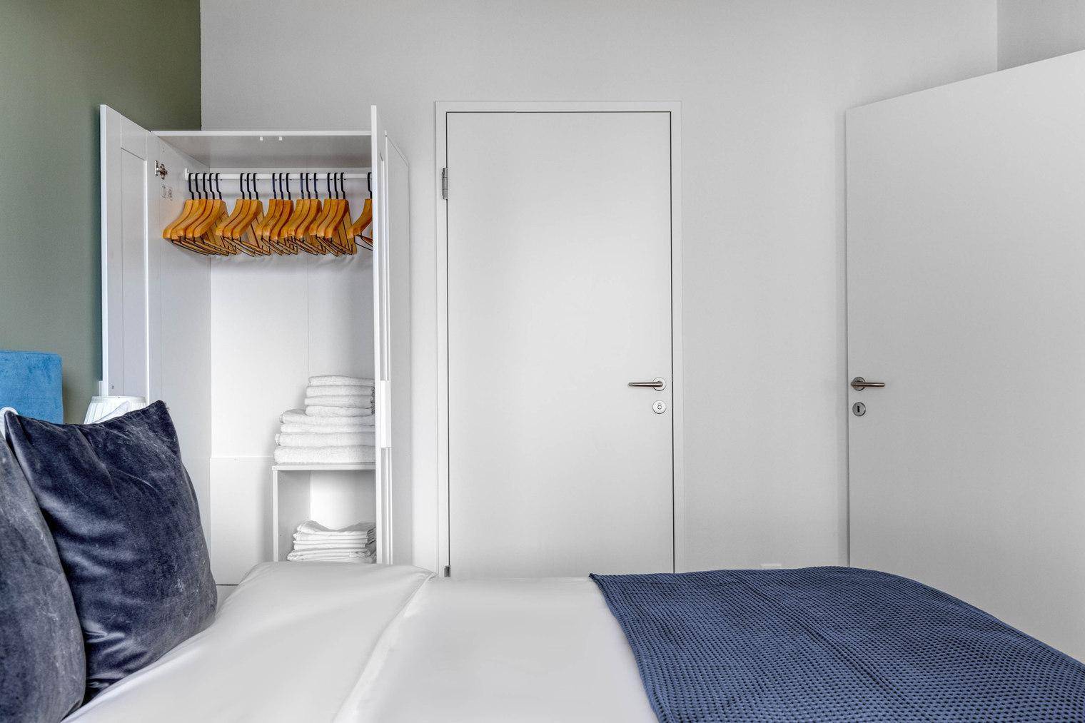 Schlafzimmer mit offenem Kleiderschrank, gefalteten Handtüchern und Holzboden.
