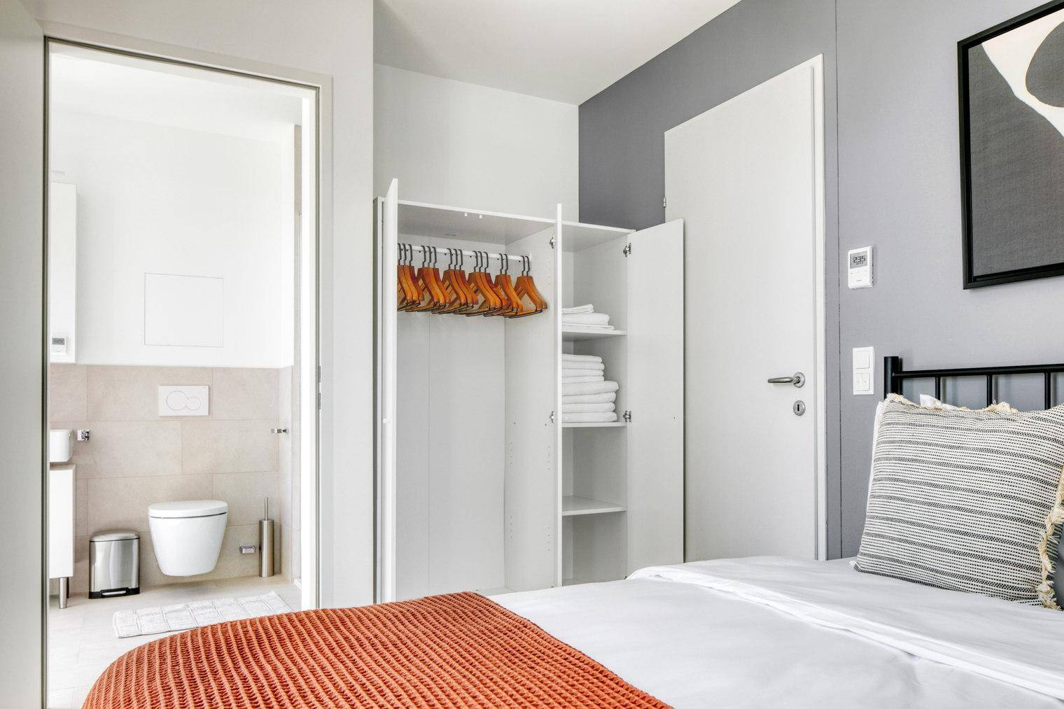 Schlafzimmer mit Zugang zum Badezimmer und offenem Kleiderschrank.