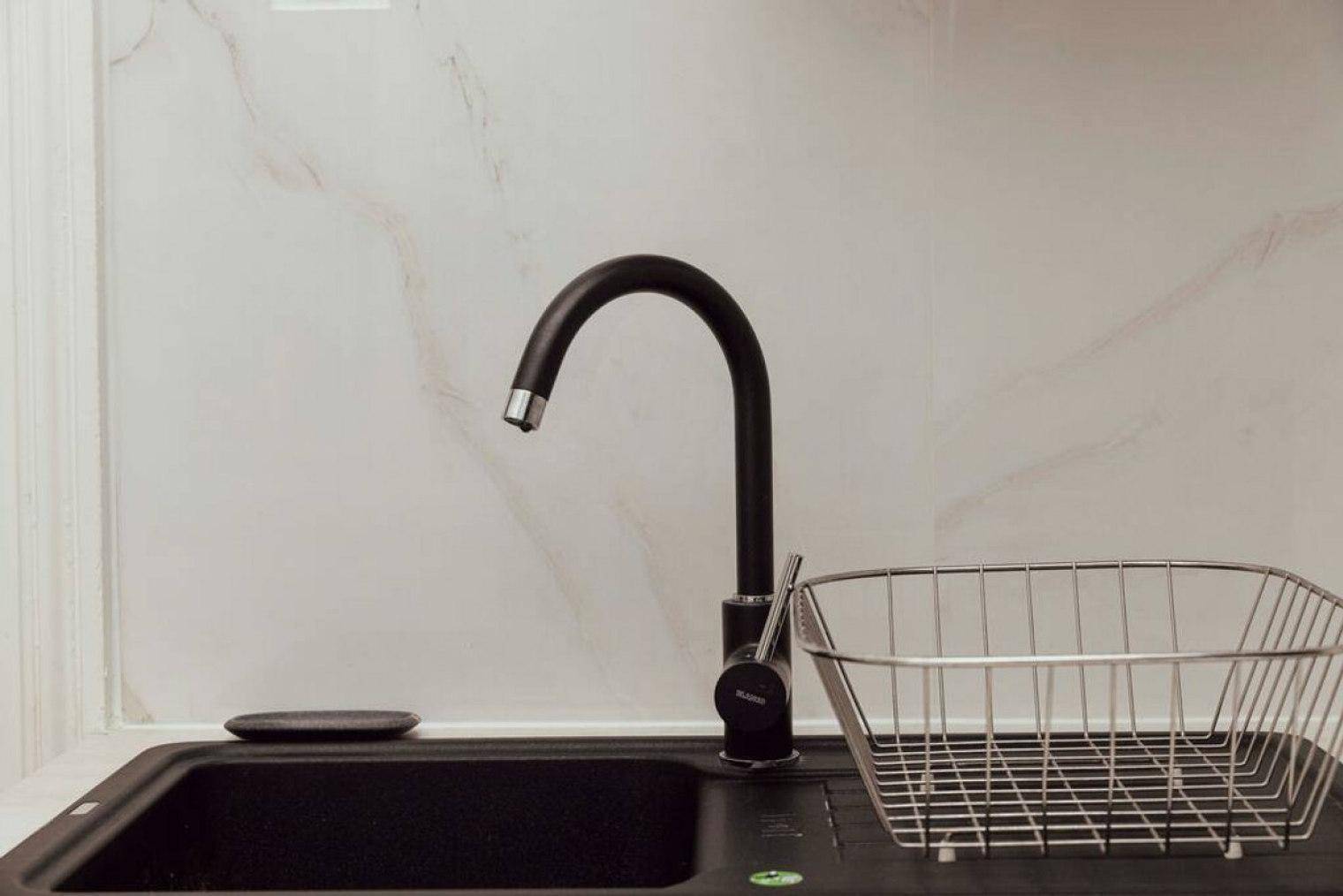 Detailansicht einer modernen schwarzen Spüle mit Wasserhahn und Abtropfkorb in der Küche.