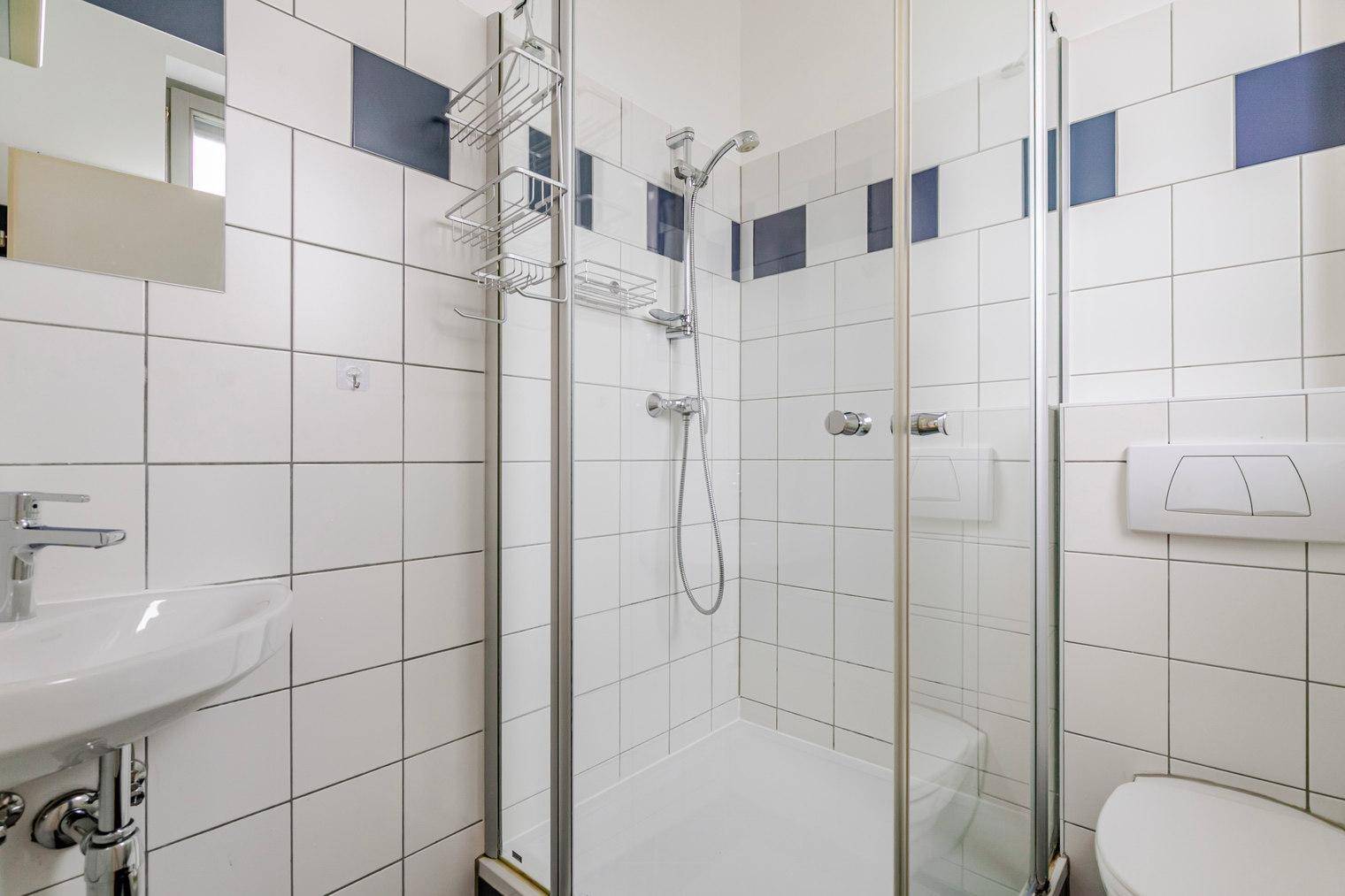 Modernes Badezimmer mit Duschkabine, Waschbecken und Toilette, weiß gefliest.