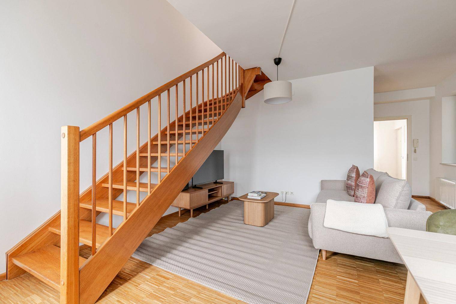 Heller Wohnbereich mit Holzboden, Teppich und einer eleganten Holztreppe.