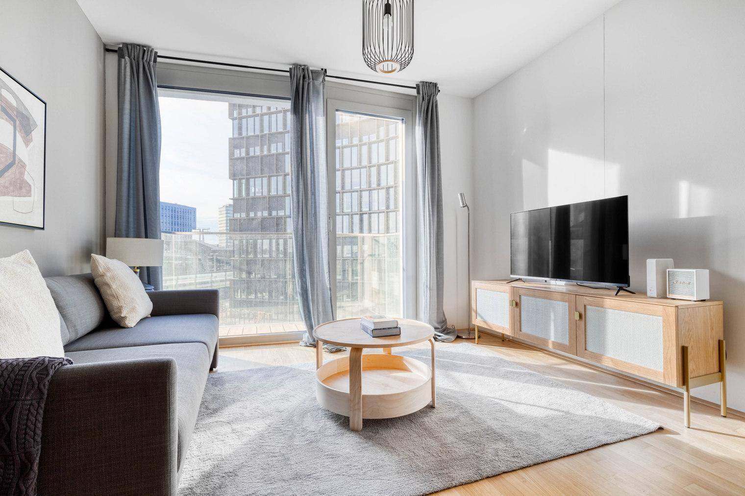 Lichtdurchflutetes Wohnzimmer mit bequemer Couch, Holzboden und Blick auf die Stadt.