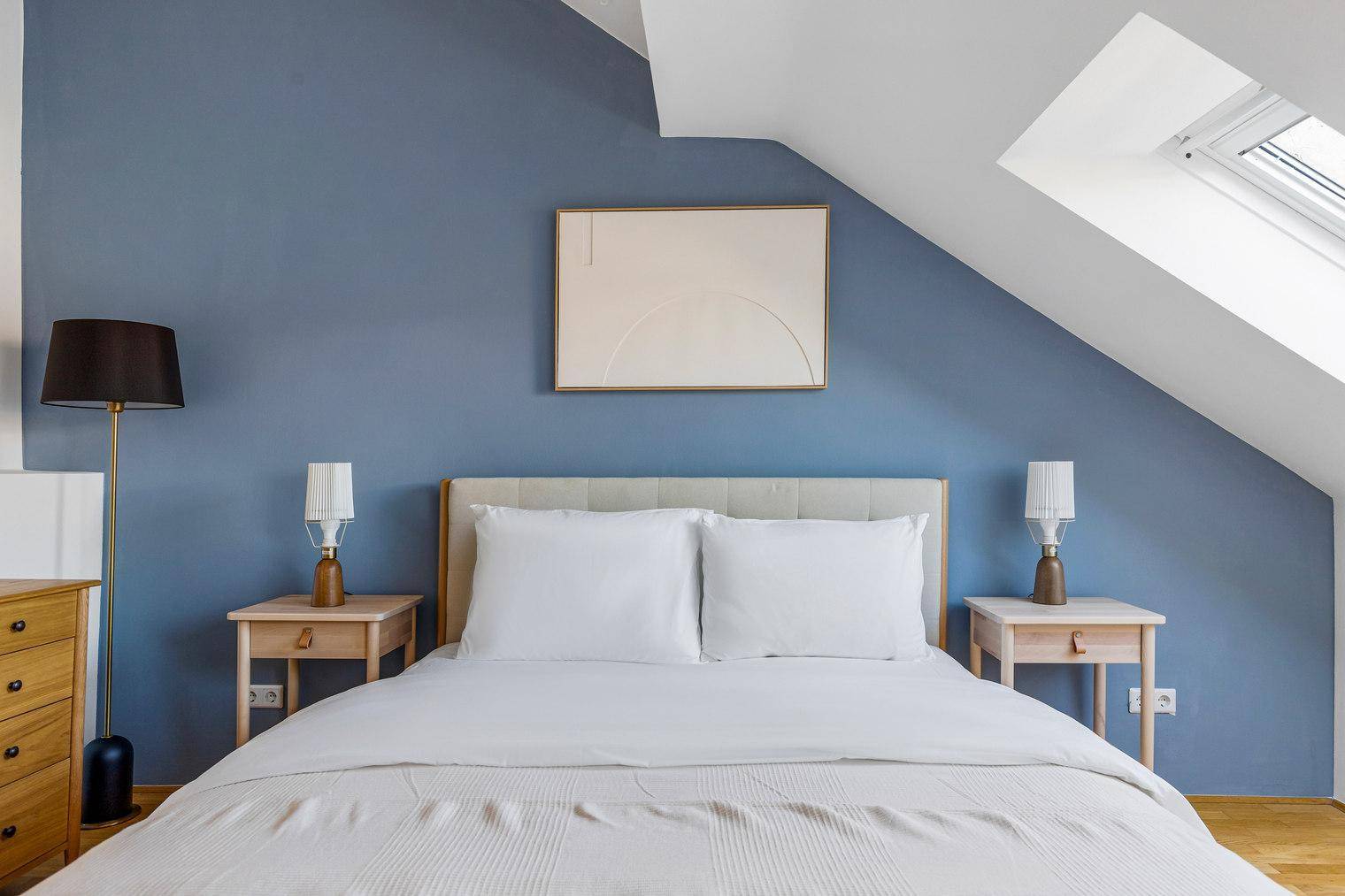 Komfortables Doppelbett im Schlafzimmer mit blauer Wand, Nachttischen und Leselampen.