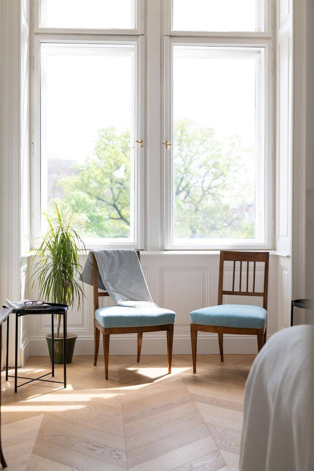 Detailansicht der hohen Fenster im Schlafzimmer mit Blick ins Grüne und zwei Stühlen.