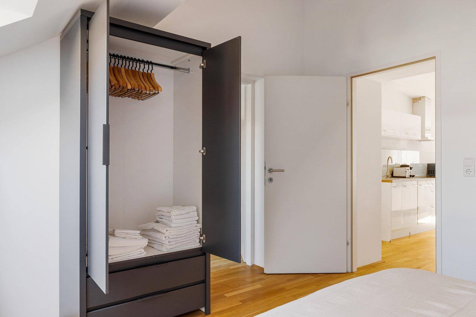 Offener Kleiderschrank im Schlafzimmer mit Kleiderbügeln und gefalteten Handtüchern.