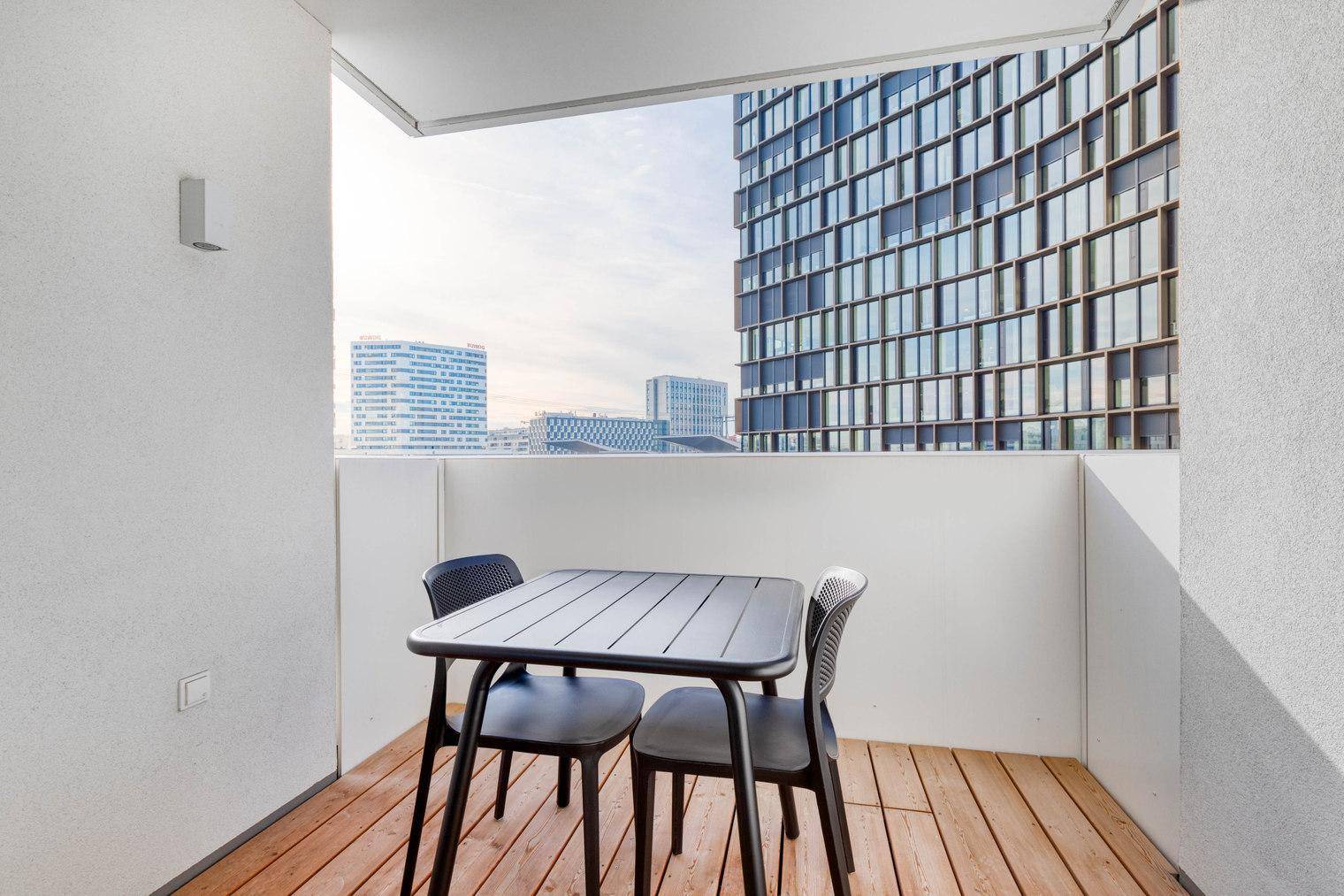 Möblierter Balkon mit Holzboden und weitem Blick auf die moderne Stadtarchitektur.