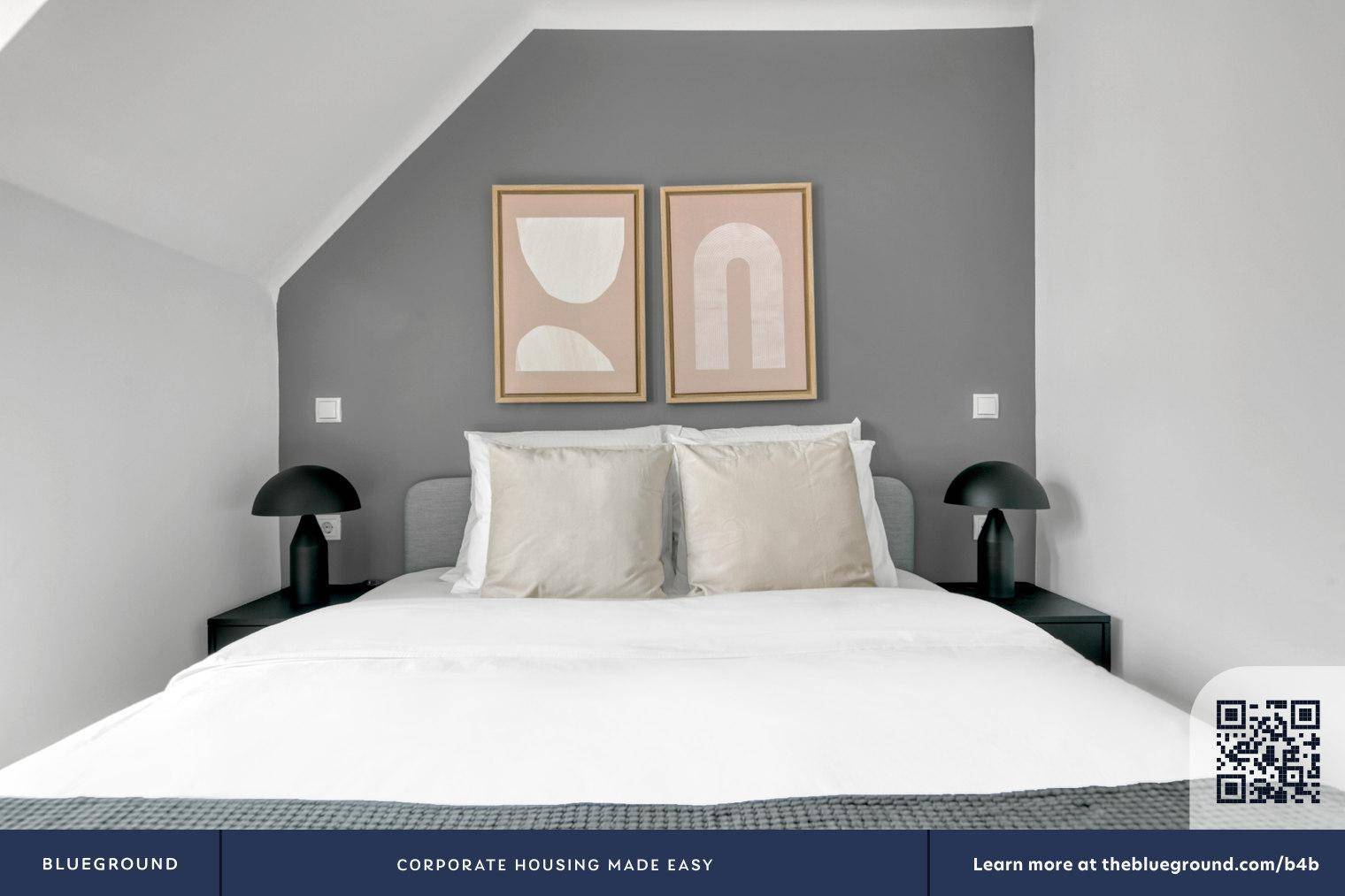 Schlafzimmer mit Doppelbett, Nachttischen und moderner Kunst an der grauen Wand.