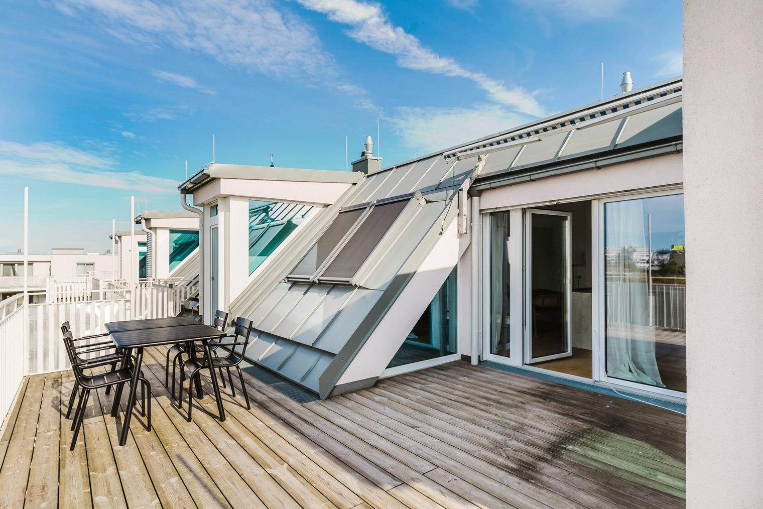 Dachterrasse mit Holzboden und Blick auf die moderne Architektur des Gebäudes und die Umgebung.