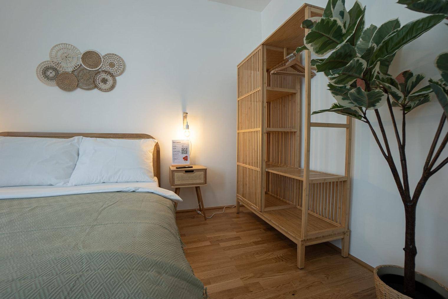 Helles Schlafzimmer mit Holzbett, offener Garderobe und großer Pflanze für eine frische Atmosphäre.