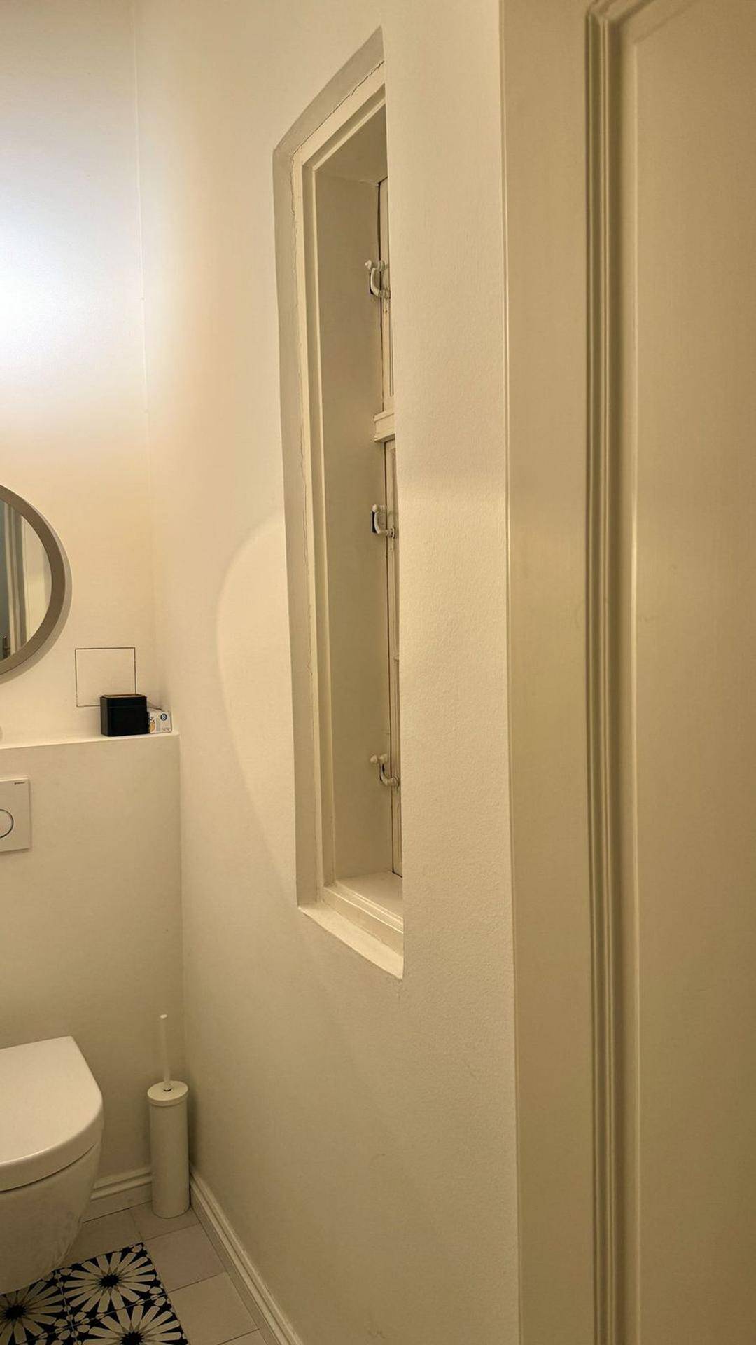 Helles Gäste-WC mit wandmontierter Toilette und schmalem Fenster für Tageslicht.