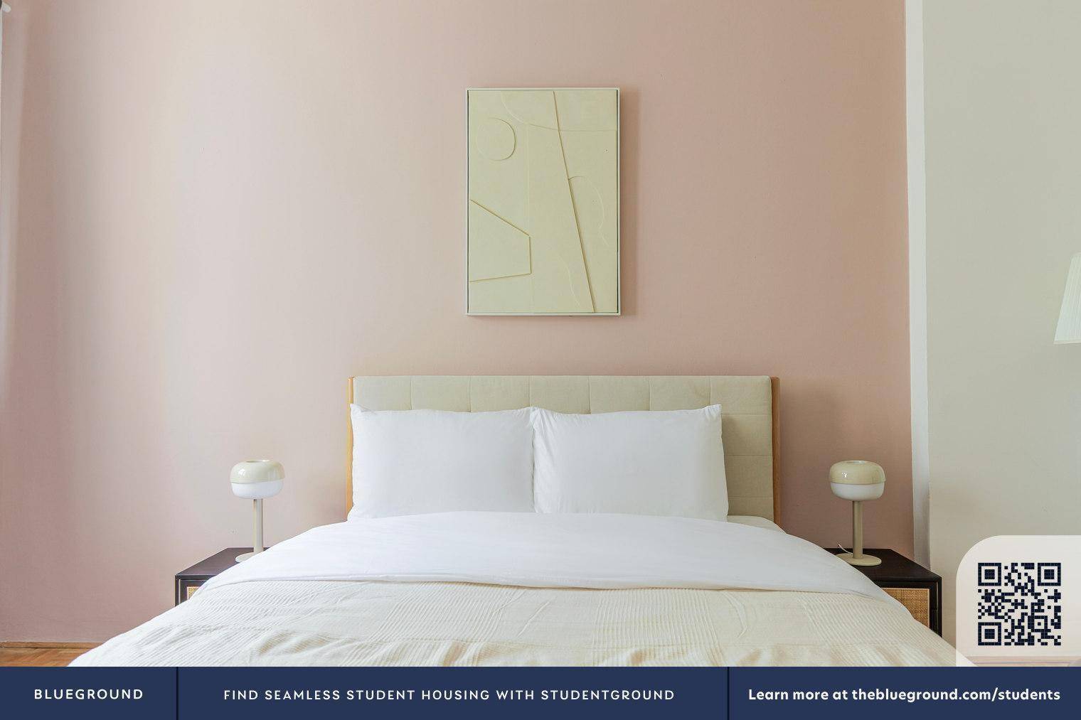 Nahaufnahme des Doppelbettes mit weißen Kissen und Nachttischen vor einer rosafarbenen Wand.