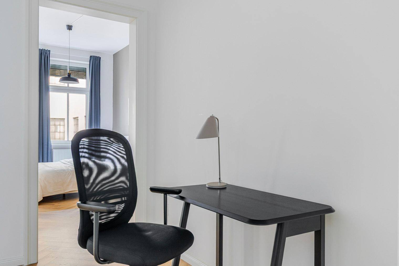 Heller Arbeitsbereich mit modernem Schreibtisch und Blick in ein angrenzendes Schlafzimmer.