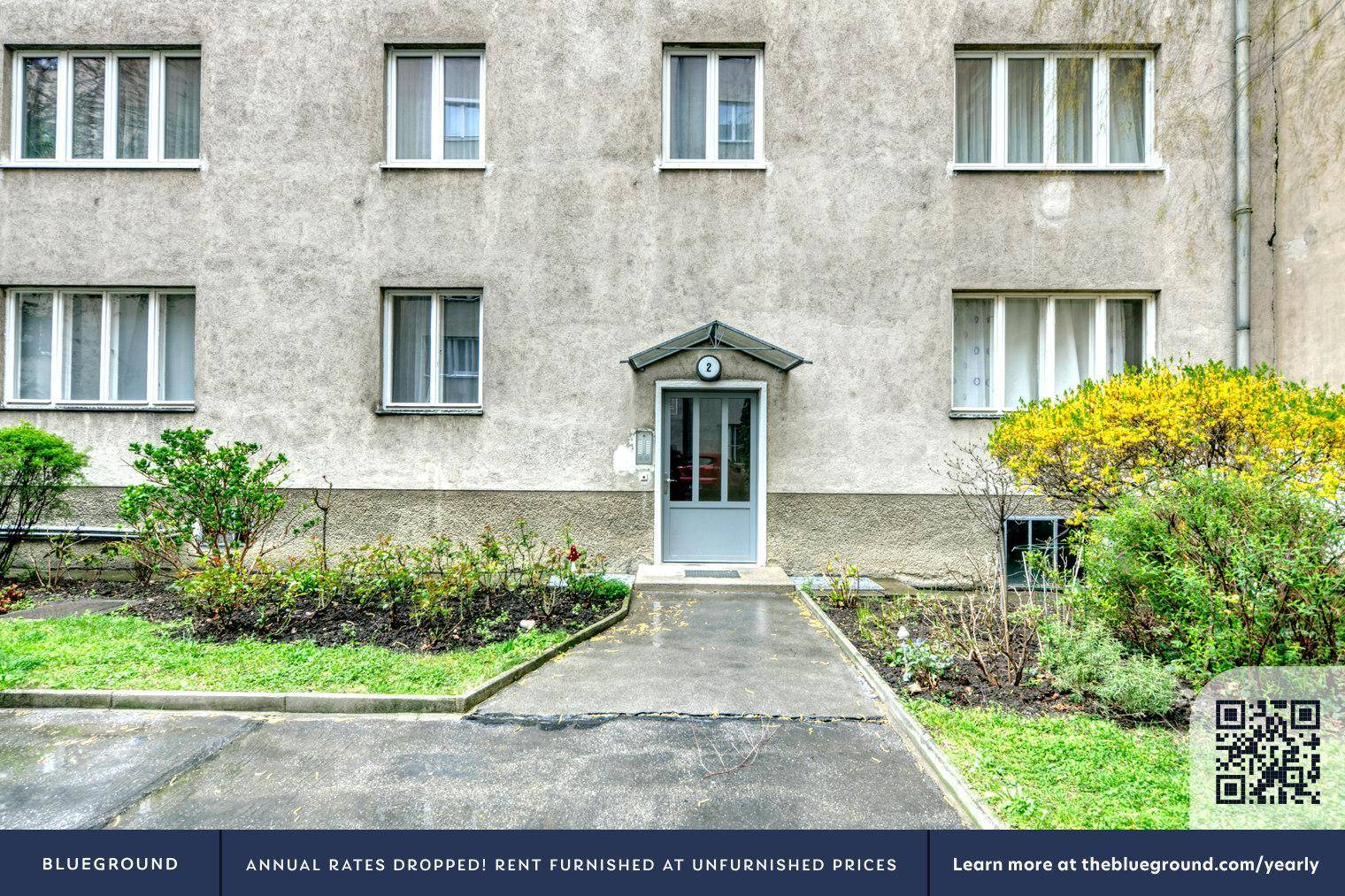 Eingangsbereich eines Mehrfamilienhauses mit gepflegtem Vorgarten und Zugangstür.