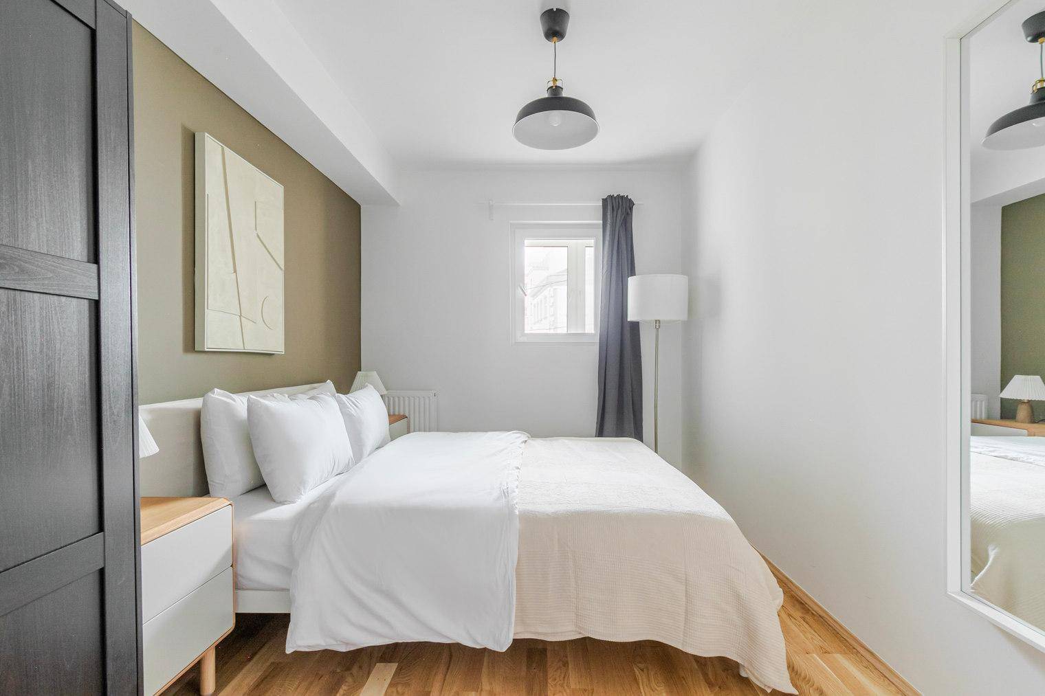 Helles Schlafzimmer mit Doppelbett, Nachttischen und einem kleinen Fenster mit Vorhang.