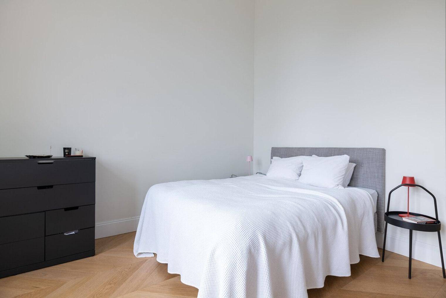 Ruhiges Schlafzimmer mit Doppelbett, minimalistischer Einrichtung und dunklem Sideboard.