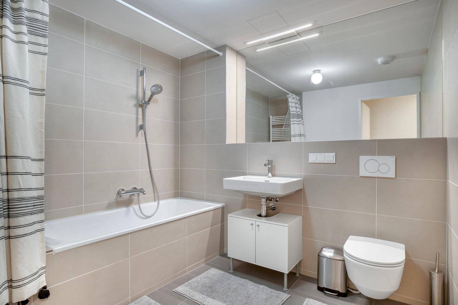 Modernes Badezimmer mit Badewanne, Dusche, Waschbecken und Wand-WC in hellen Fliesen.