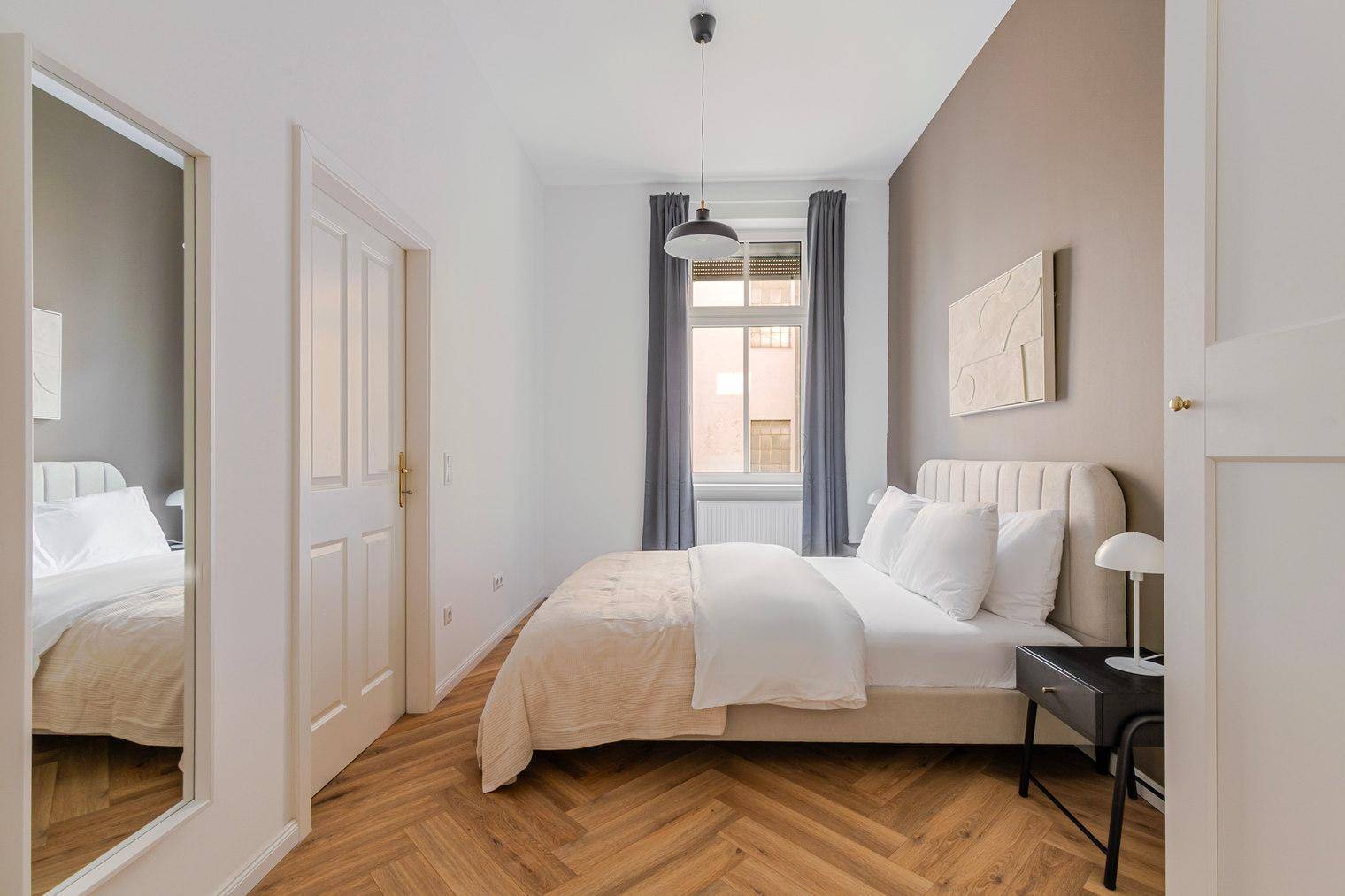 Gemütliches Schlafzimmer mit Doppelbett, Fischgrätparkett und brauner Akzentwand.
