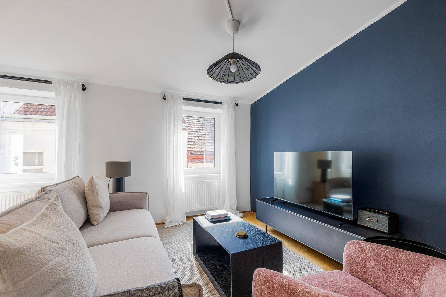 Gemütliches Wohnzimmer mit modernem Sofa, Fernseher und einer Akzentwand in Dunkelblau.