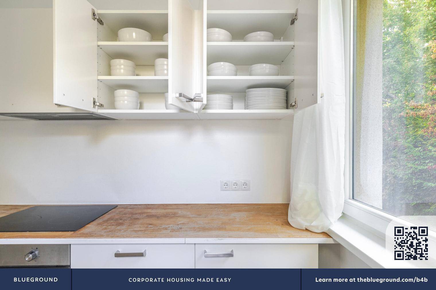 Offene Küchenschränke zeigen Geschirr und Tassen, mit einem Fenster und Kochfeld darunter.