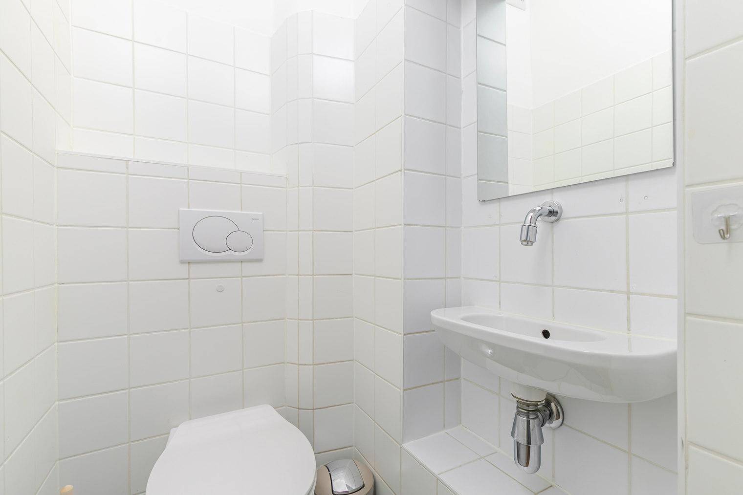 Kleines Gäste-WC mit weiß gefliesten Wänden, Toilette und Waschbecken.
