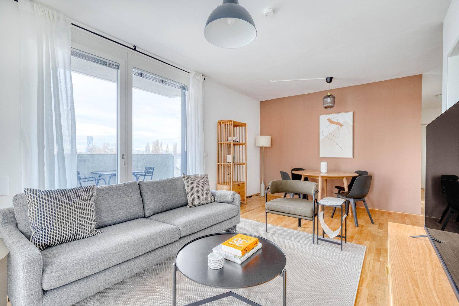 Moderner Wohn- und Essbereich mit farbiger Akzentwand und Zugang zum Balkon.