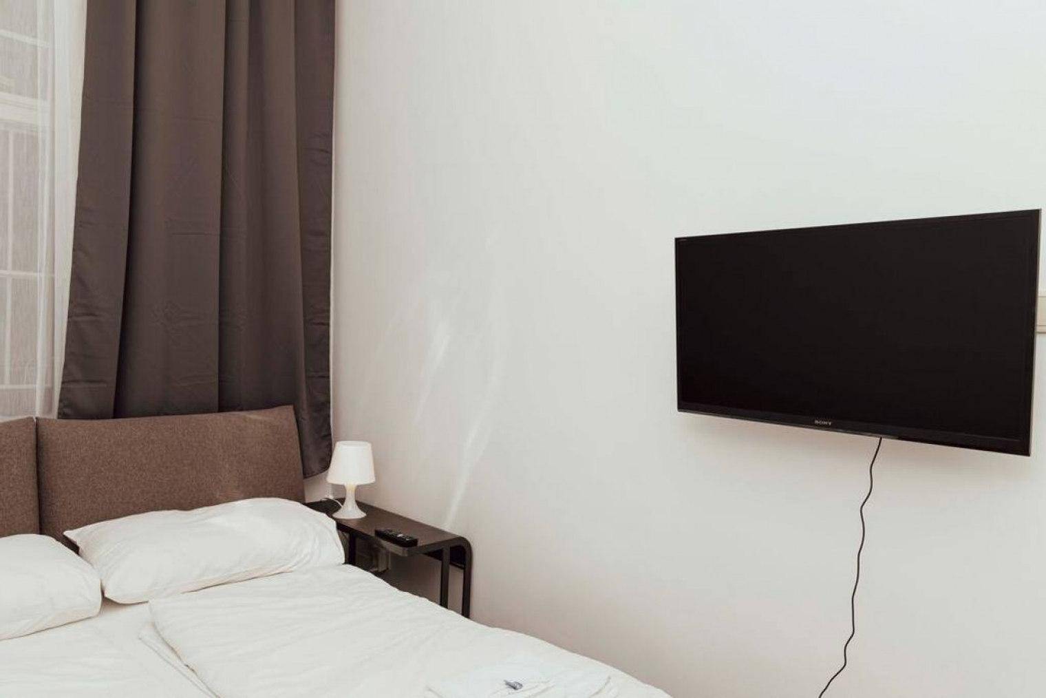 Schlafzimmer mit Doppelbett, Nachttisch und einem an der Wand montierten Fernseher.