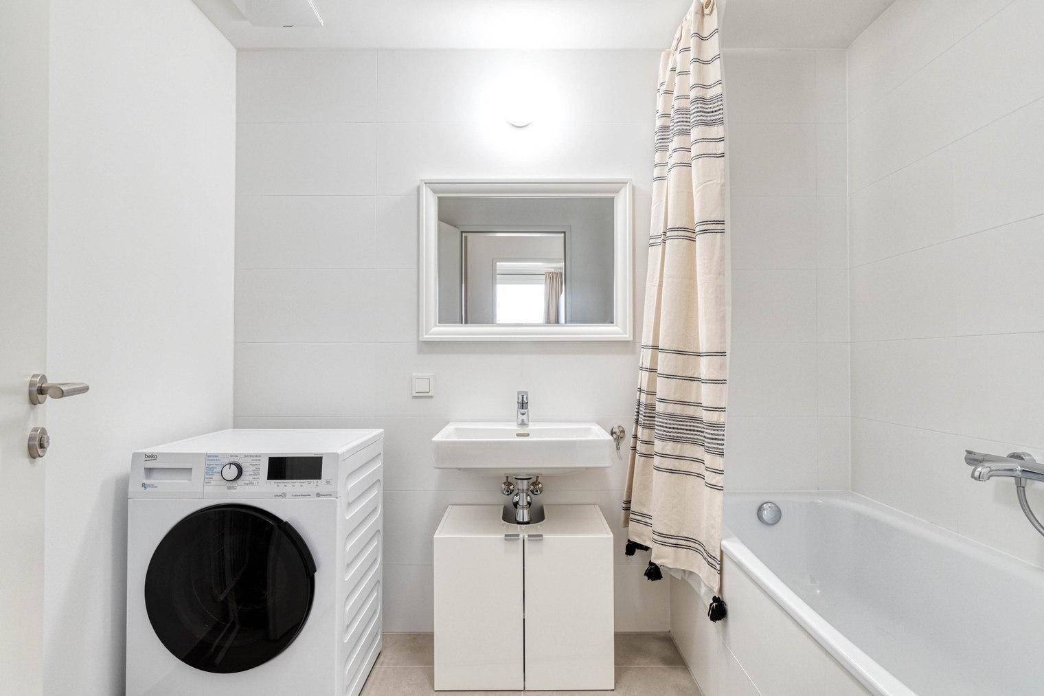 Helles Badezimmer mit Badewanne, Waschbecken und Waschmaschine.