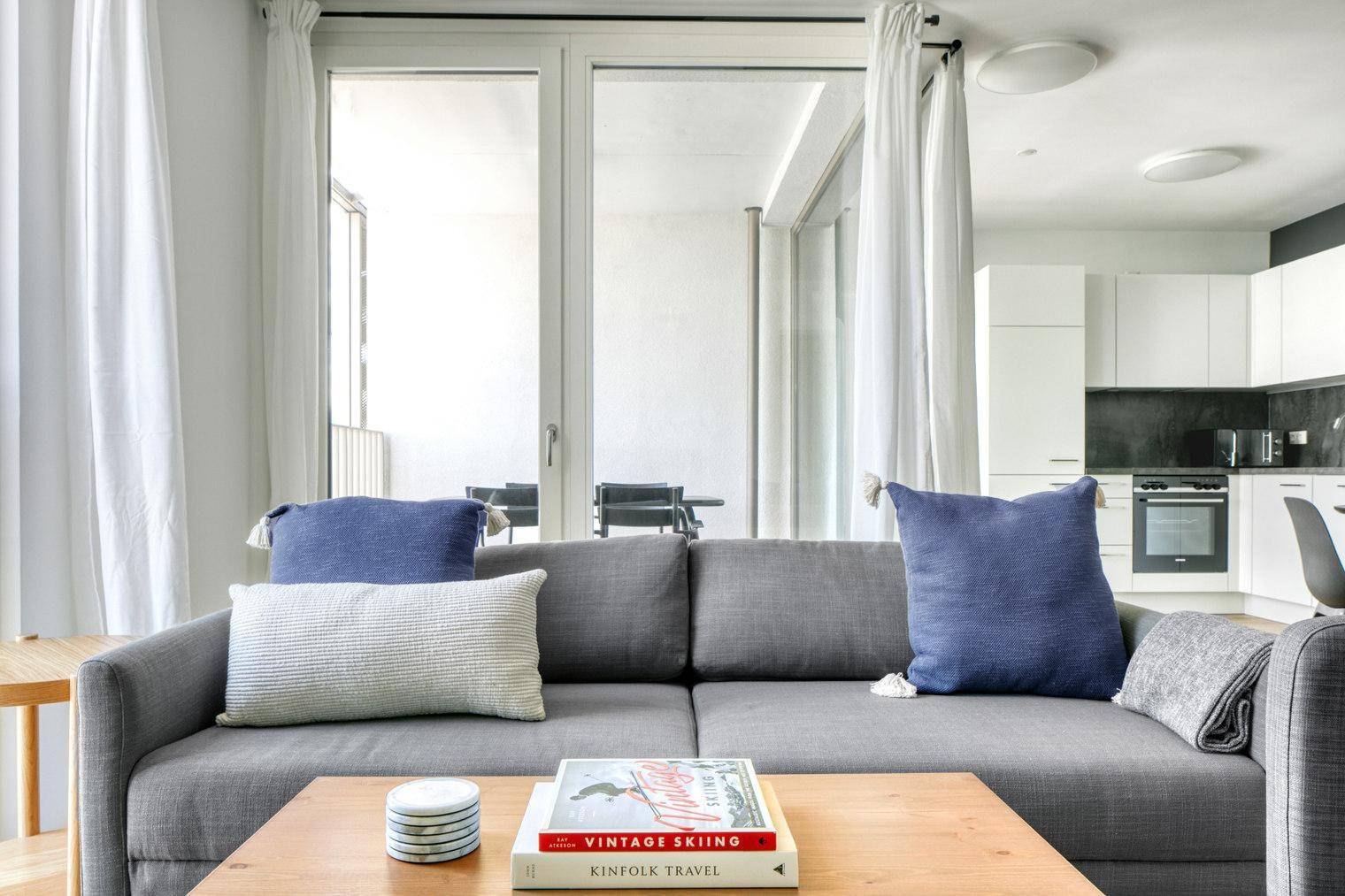 Moderner Wohnbereich mit grauem Sofa und offener Küche im Hintergrund.