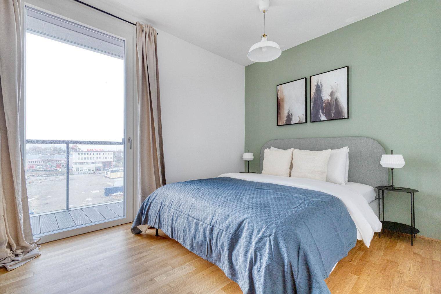 Helles Schlafzimmer mit Doppelbett, grüner Akzentwand und Balkonzugang.