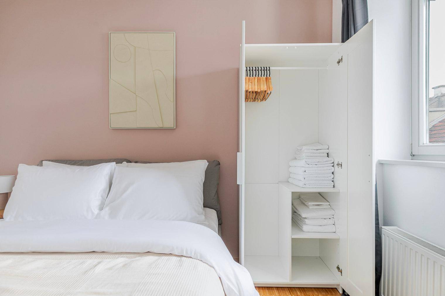 Offener Kleiderschrank mit Kleiderbügeln und gestapelter Wäsche im Schlafzimmer.