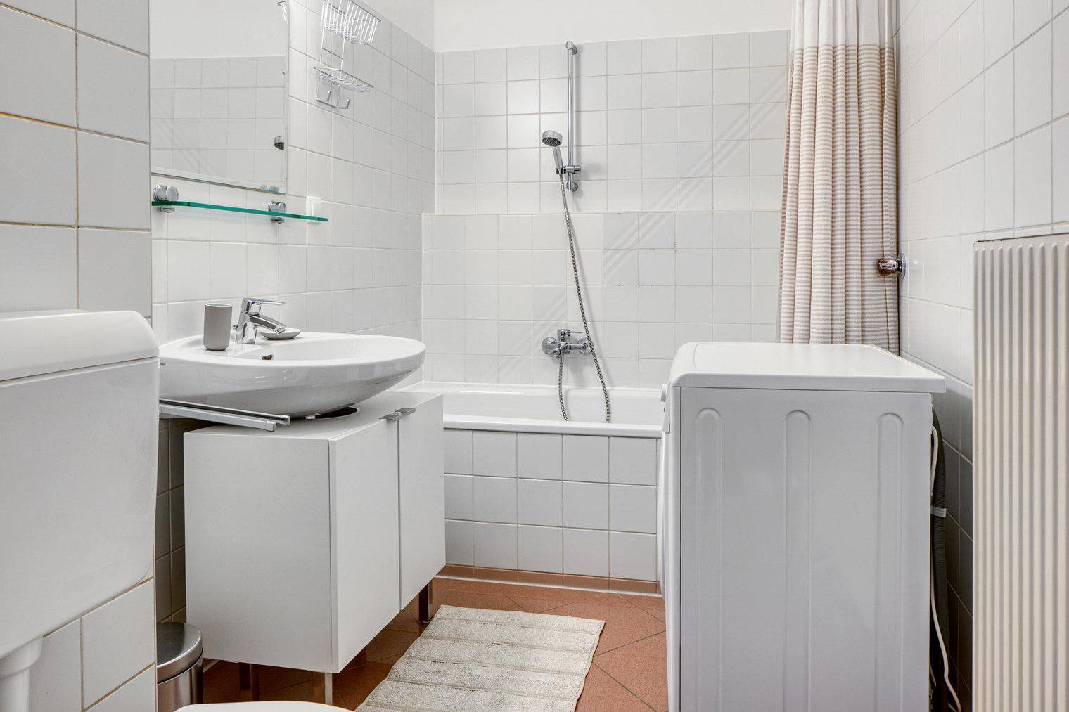 Helles Badezimmer mit Badewanne, Waschbecken und weißen Fliesen.