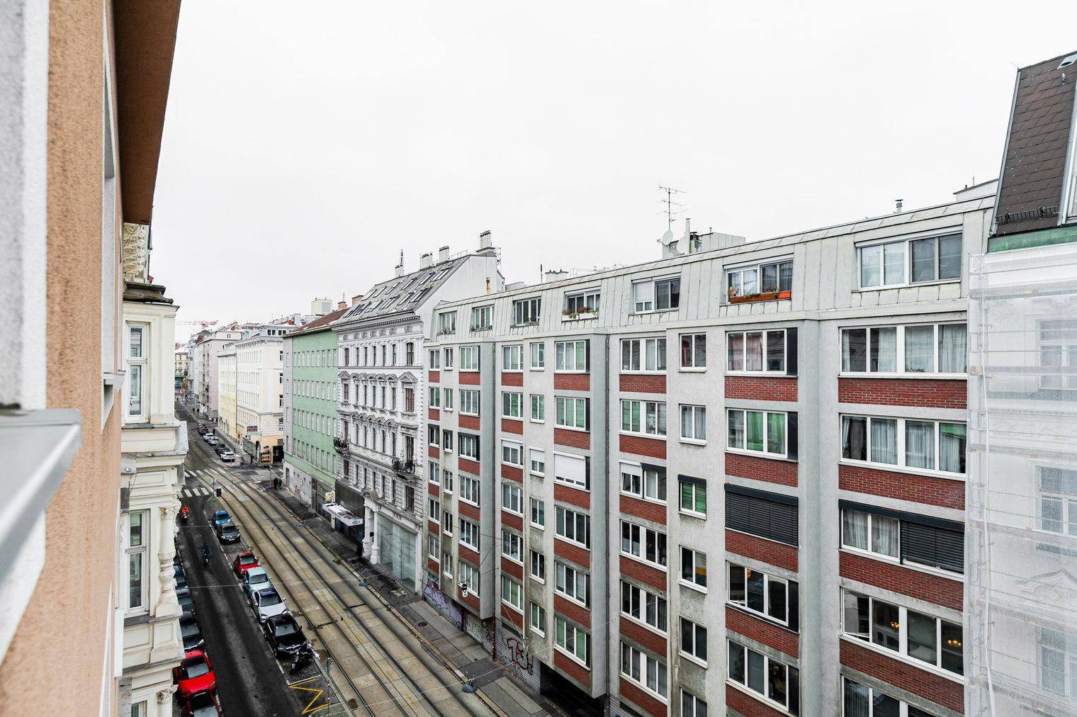 Blick von oben auf eine belebte Stadtstraße mit Straßenbahnschienen und Gebäuden.