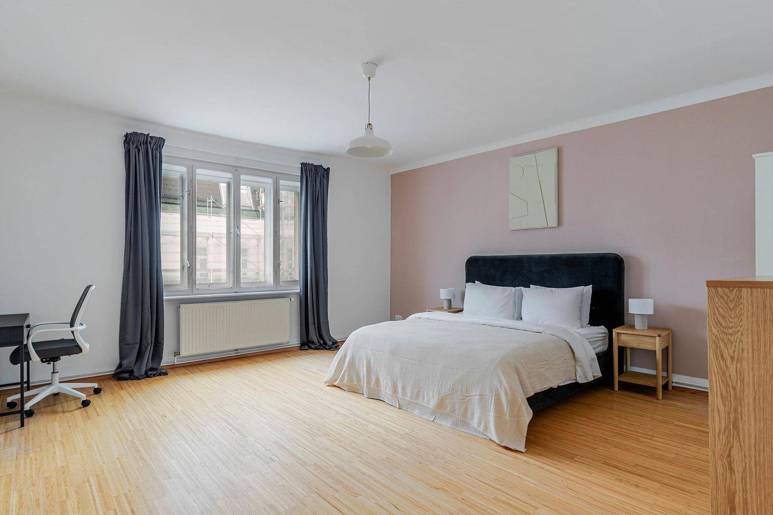 Geräumiges Schlafzimmer mit Doppelbett, Holzboden und rosa Akzentwand.