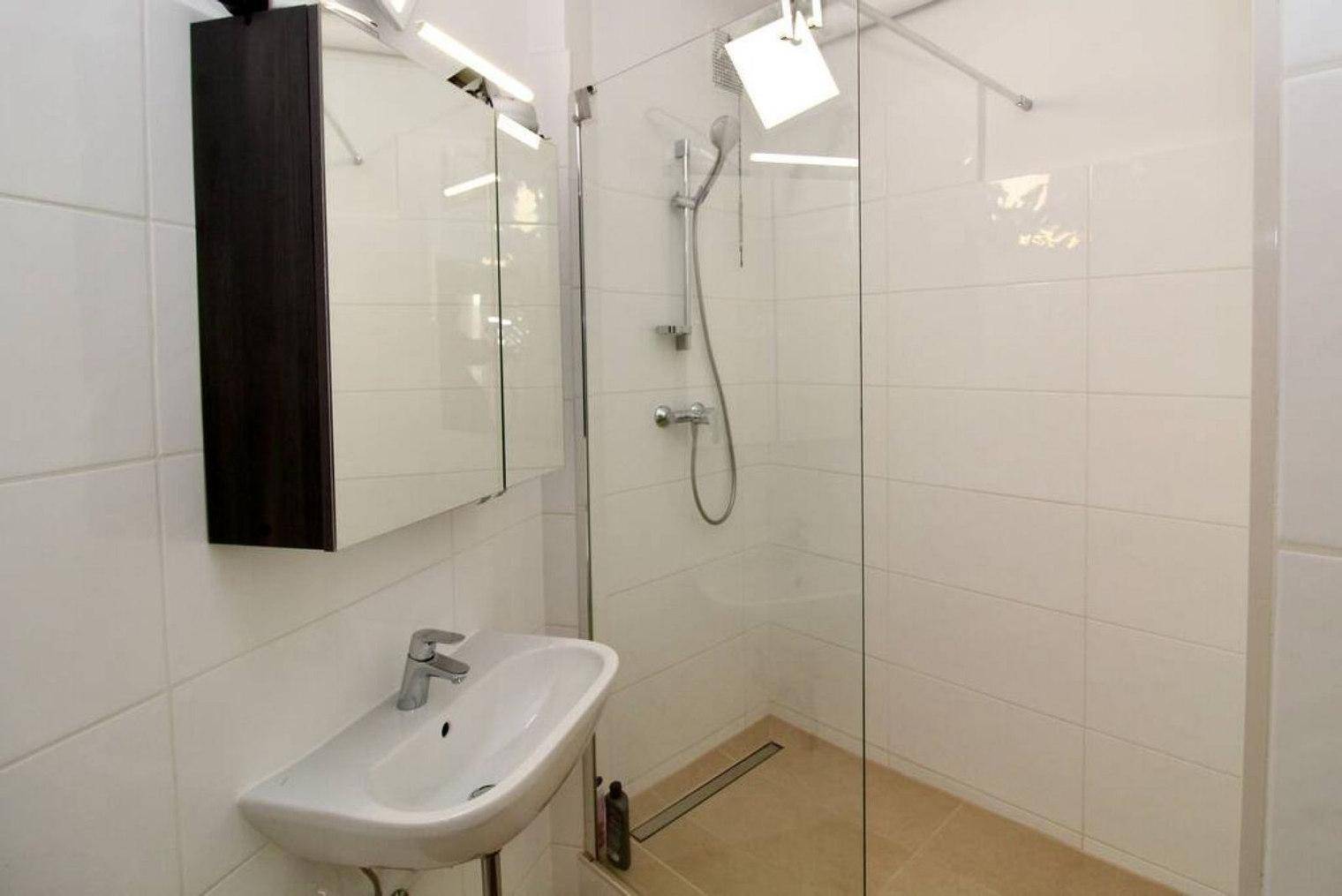 Modernes Badezimmer mit weißen Fliesen, Waschbecken und ebenerdiger Dusche.