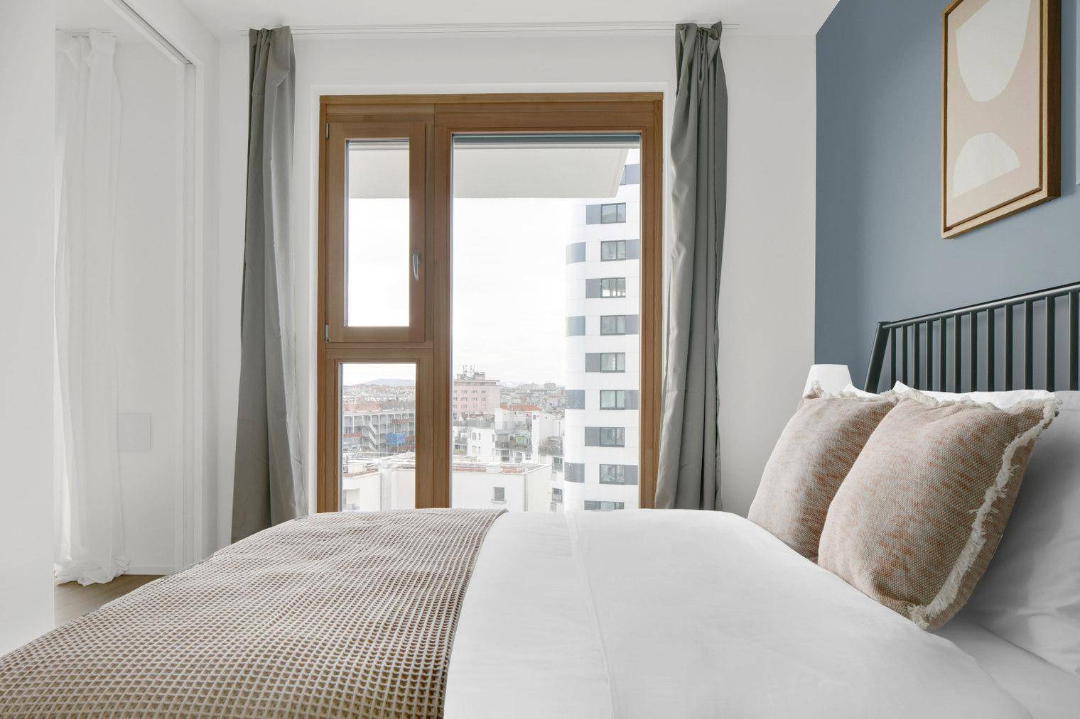 Helles Schlafzimmer mit großem Fenster, Blick auf die Stadt und moderne Einrichtung.