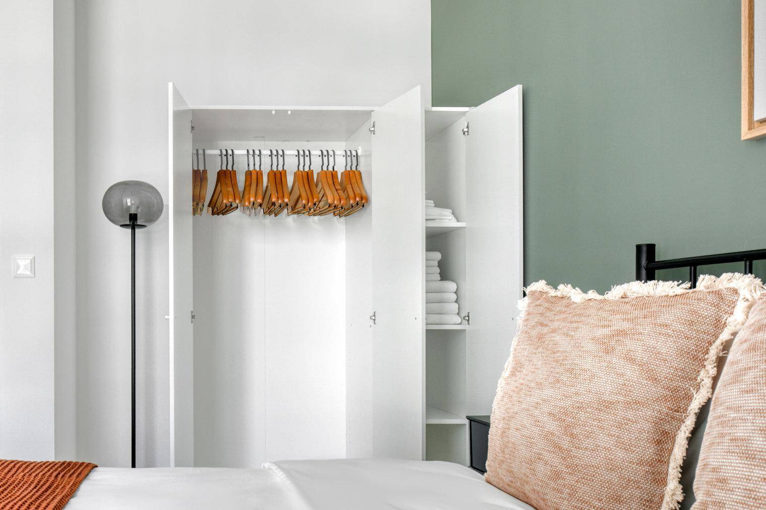 Schlafzimmer mit offenem Kleiderschrank, Holzboden und moderner Stehlampe.