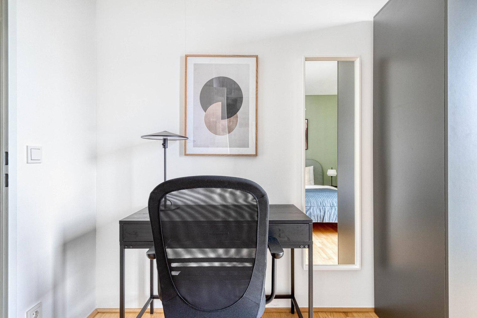 Arbeitsbereich im Schlafzimmer mit Schreibtisch, Stuhl und modernem Wandbild.
