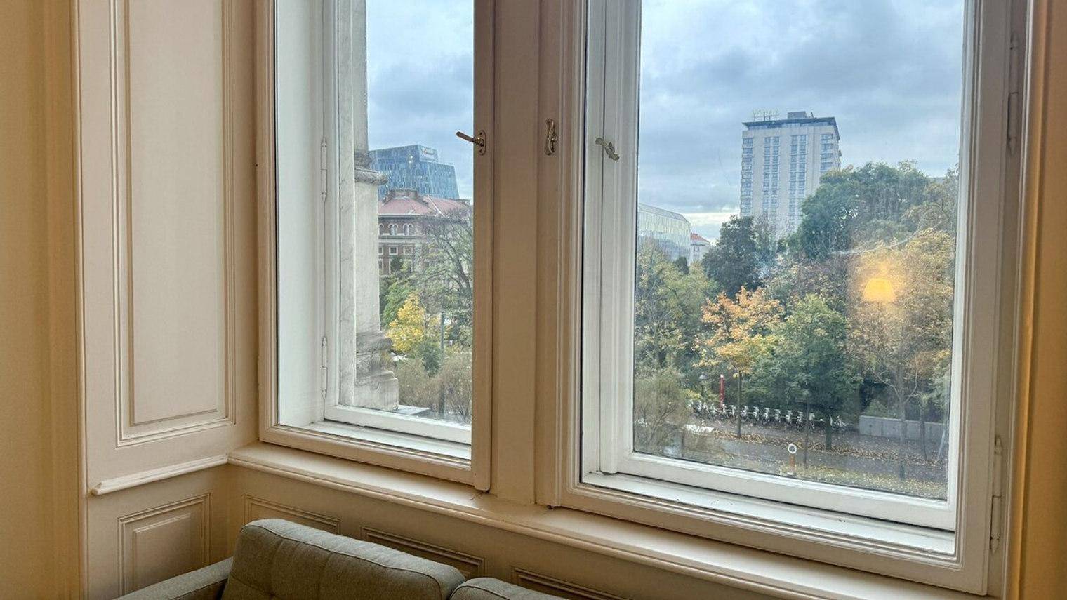 Wohnzimmer mit großzügigen Fenstern, die einen Blick auf Bäume und Stadtgebäude bieten.