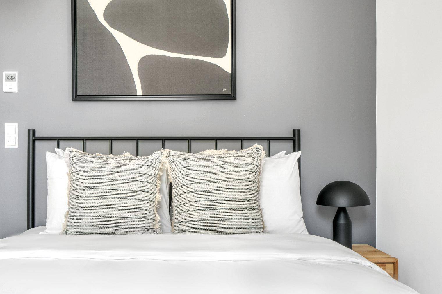 Gemütliches Schlafzimmer mit Doppelbett, modernem Kopfteil und Kunstwerk an der Wand.