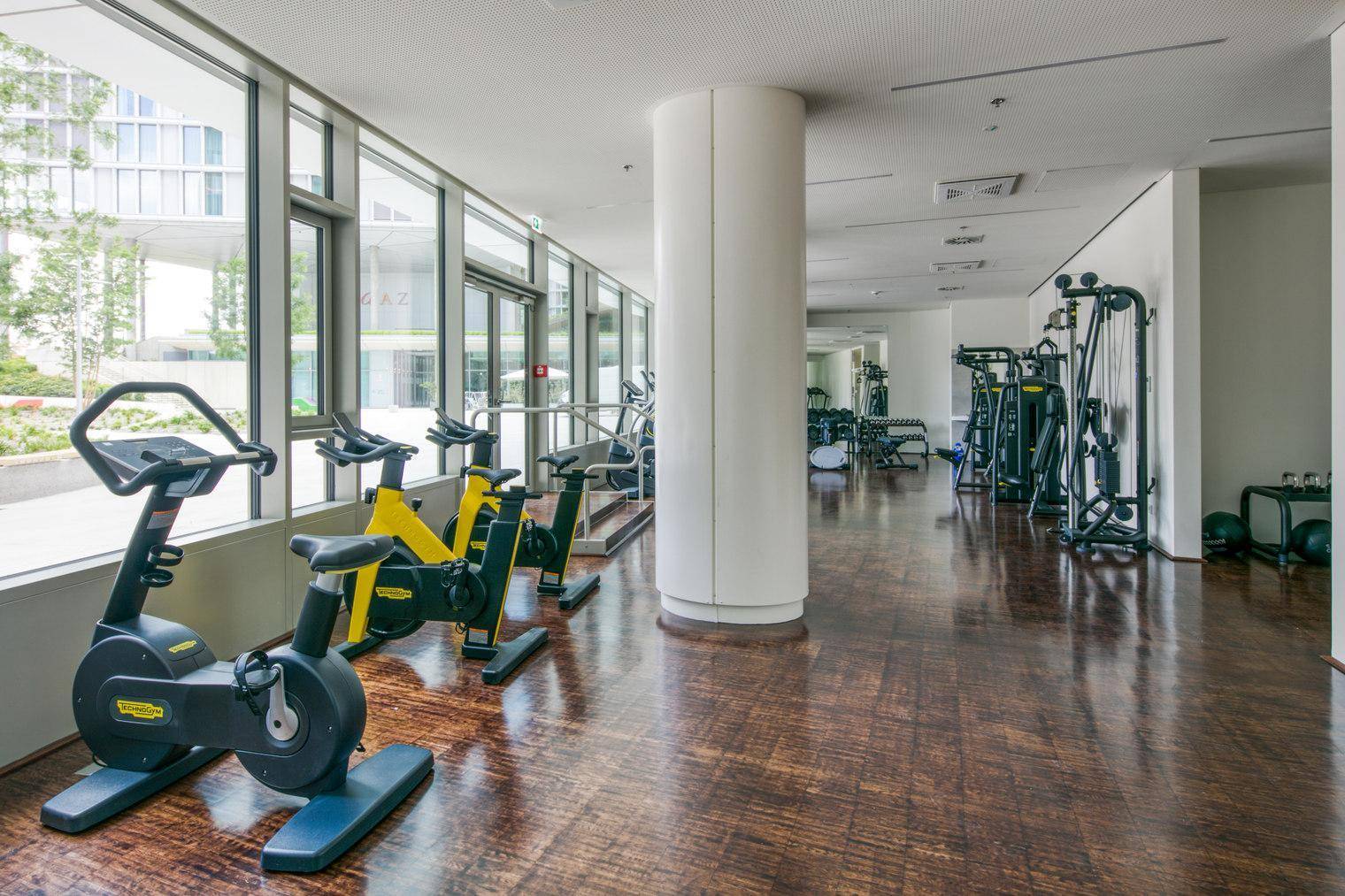 Moderner Fitnessraum mit verschiedenen Trainingsgeräten und großen Fenstern.