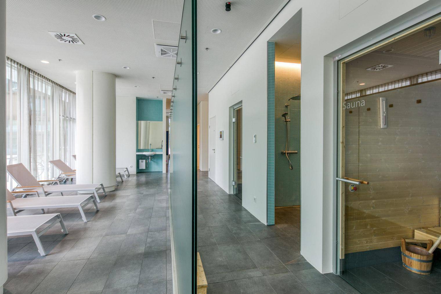 Entspannender Wellnessbereich mit Liegestühlen, Sauna und Duschkabinen.